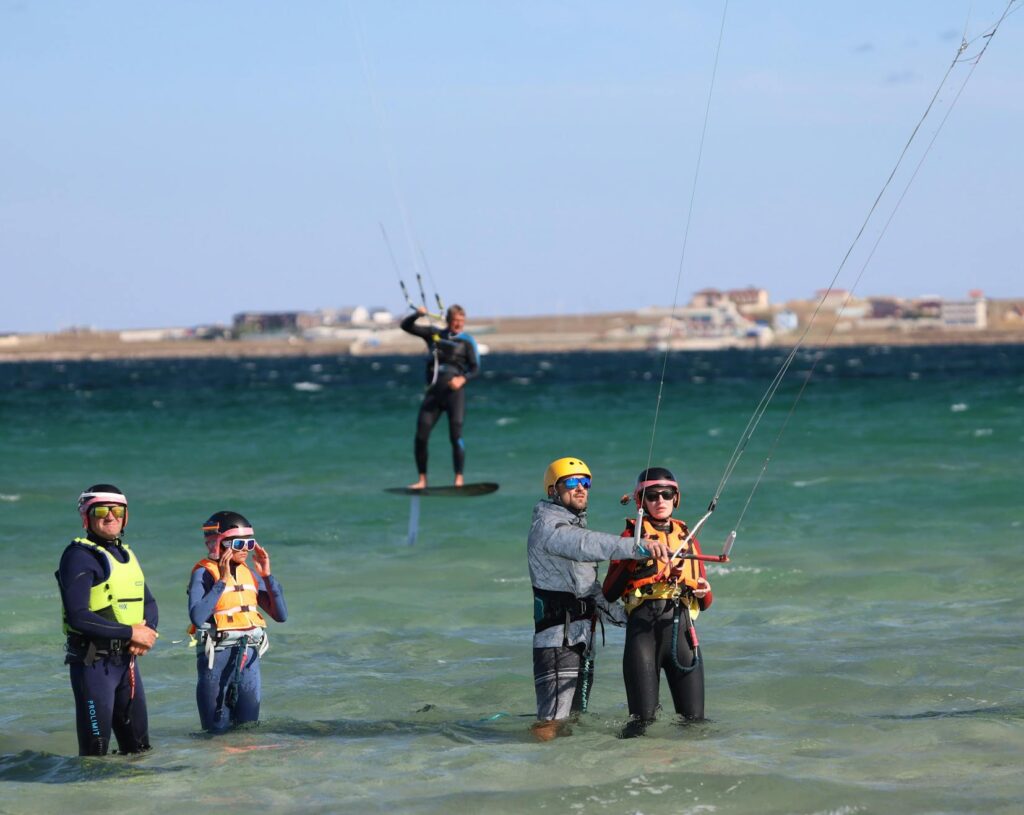 Instructors teaching kitesurfing in shallow sea waters with clear skies, offering a perfect leisure activity.