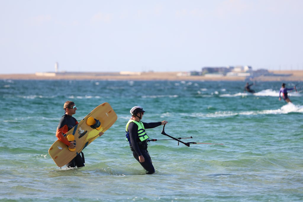 Two men kiteboarding in wetsuits, enjoying a sunny day at the beach.