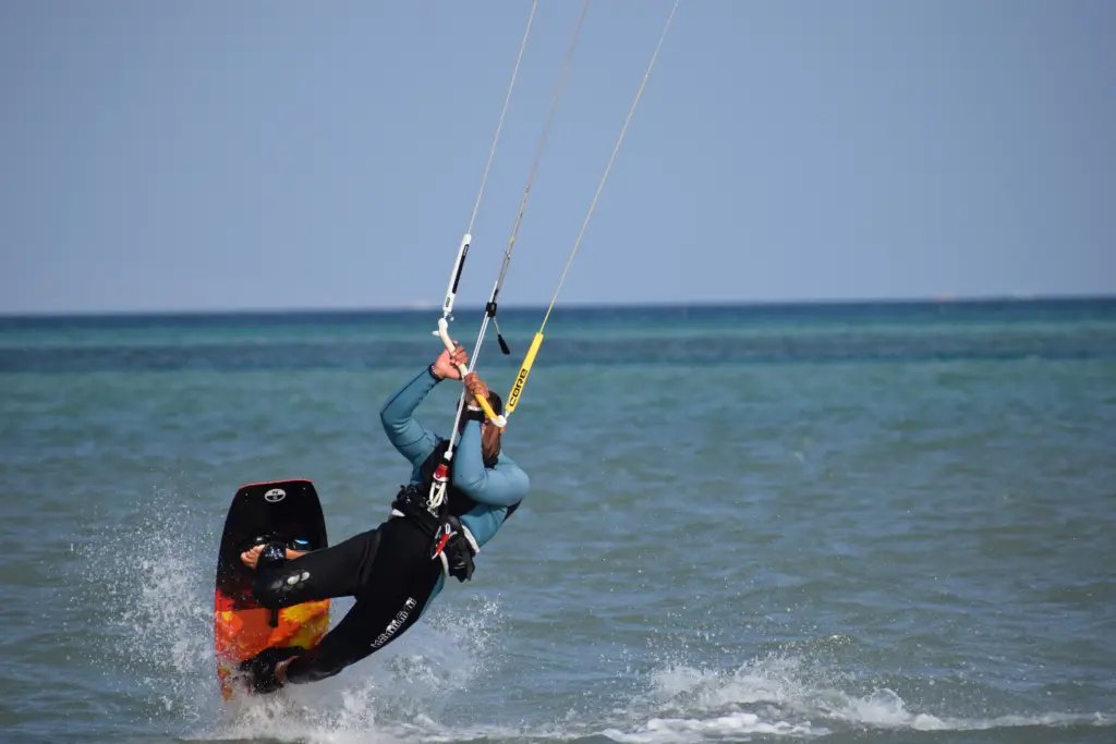Kitesurfer riding in shallow sea water while pulling the kite, with the board partially lifting out of the water. Kitesurfer fährt im flachen Meerwasser und zieht mit dem Kite an, das Board hebt sich teilweise aus dem Wasser.