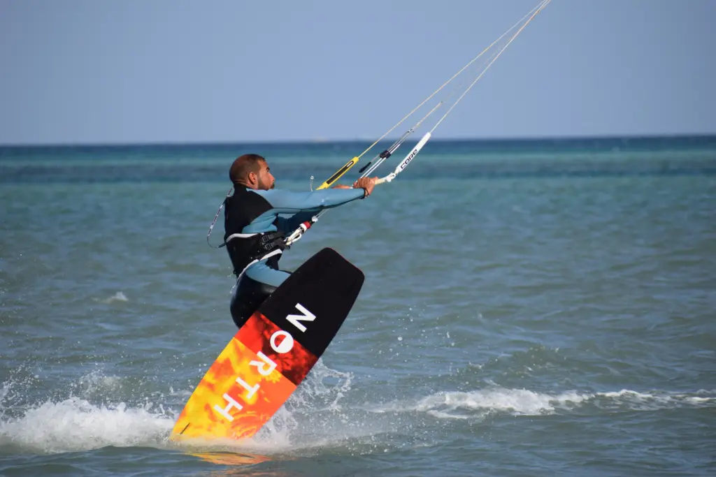Kitesurfer riding in shallow sea water while pulling the kite, with the board partially lifting out of the water. Kitesurfer fährt im flachen Meerwasser und zieht mit dem Kite an, das Board hebt sich teilweise aus dem Wasser.